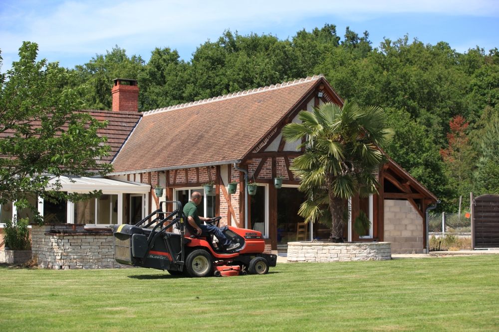 Homme tondant la pelouse devant une maison